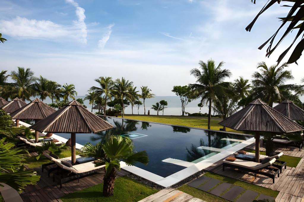 Scenic outdoor infinity pool surrounded by palm trees and sun loungers at Vedana Lagoon Resort Vietnam facing the peaceful lagoon.