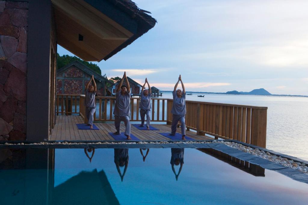 Guests practice sunrise yoga on a wooden deck over the water at Vedana Lagoon Resort Vietnam, surrounded by serene lagoon views.