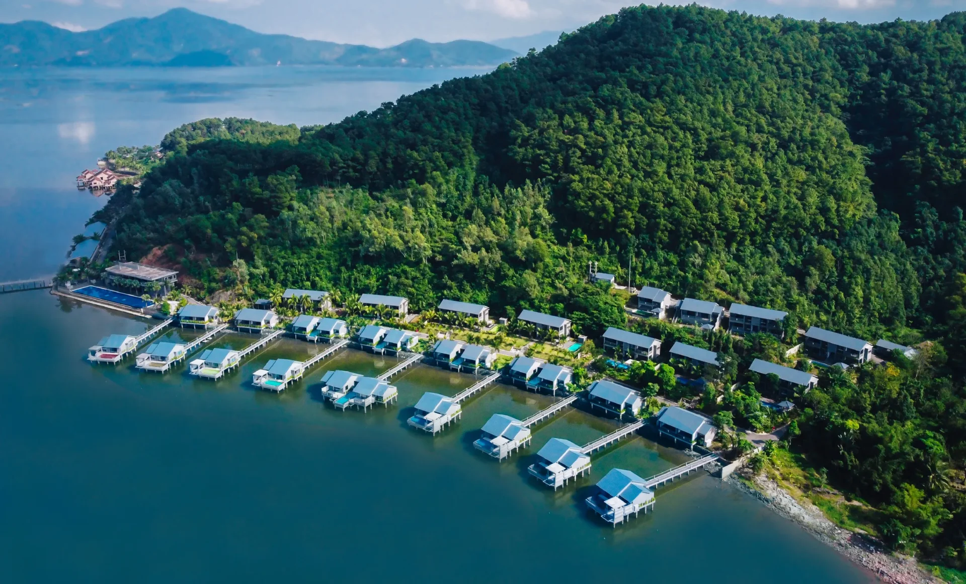 Aerial view of Vedana Lagoon Resort Vietnam with over-water villas surrounded by lush green hills and calm lagoon.