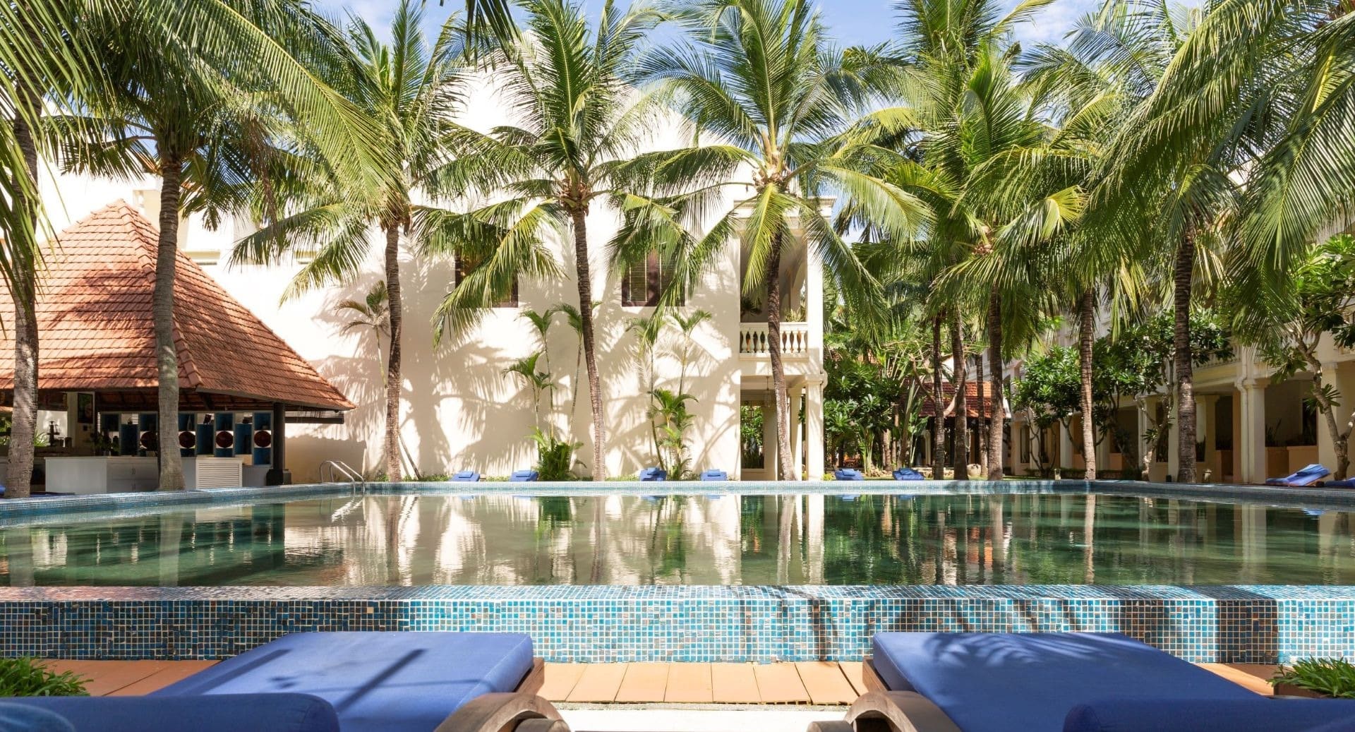 Palm-shaded swimming pool with sun loungers and colonial architecture at Anantara Hoi An Resort in Vietnam.