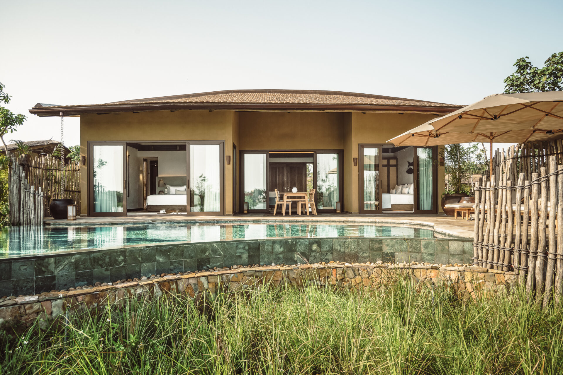Private villa at Namia River Retreat with infinity pool, modern architecture, lush greenery, and open glass-fronted design. 