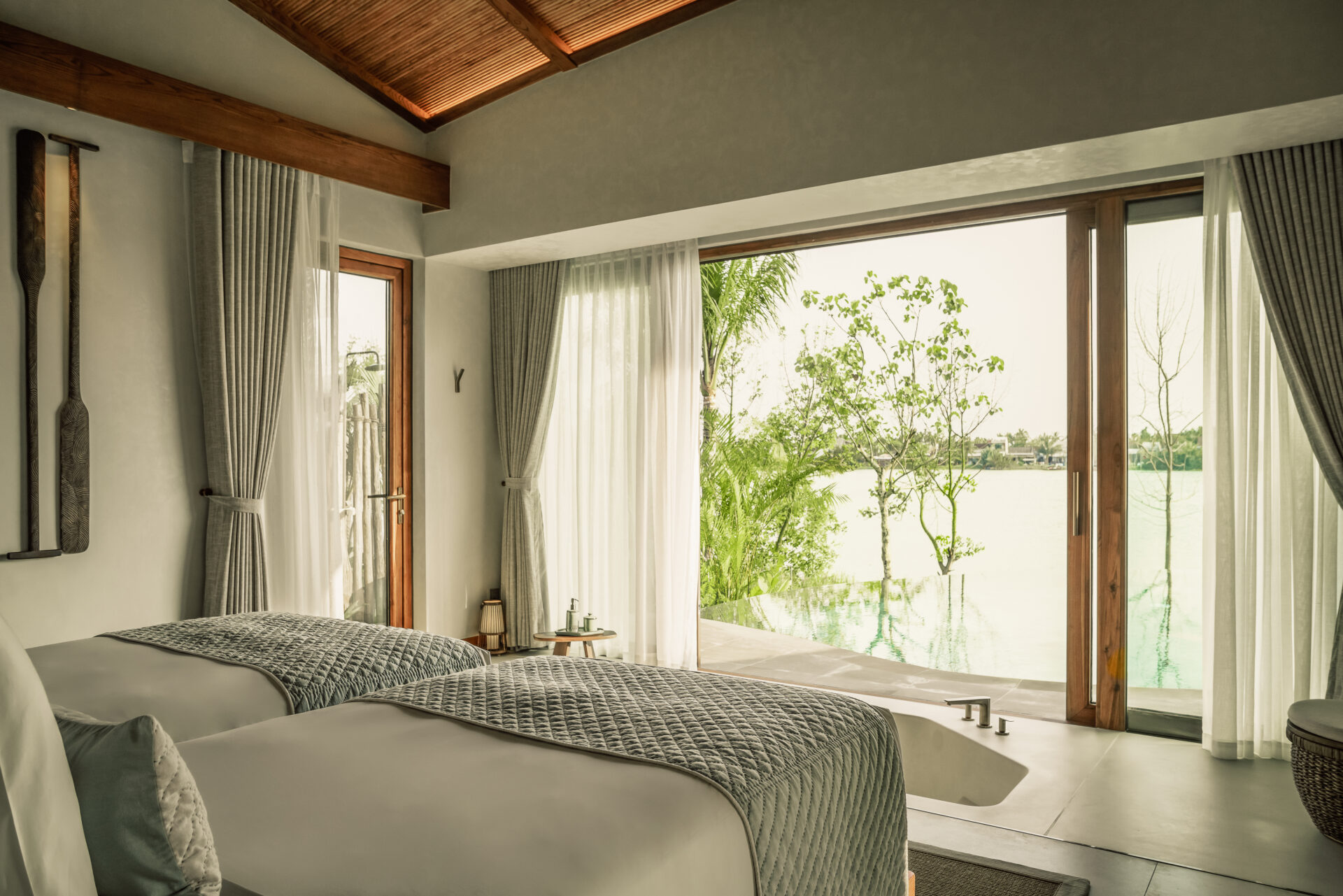Twin bedroom at Namia River Retreat with soft lighting, large windows, river view, and soothing minimalist interior design.