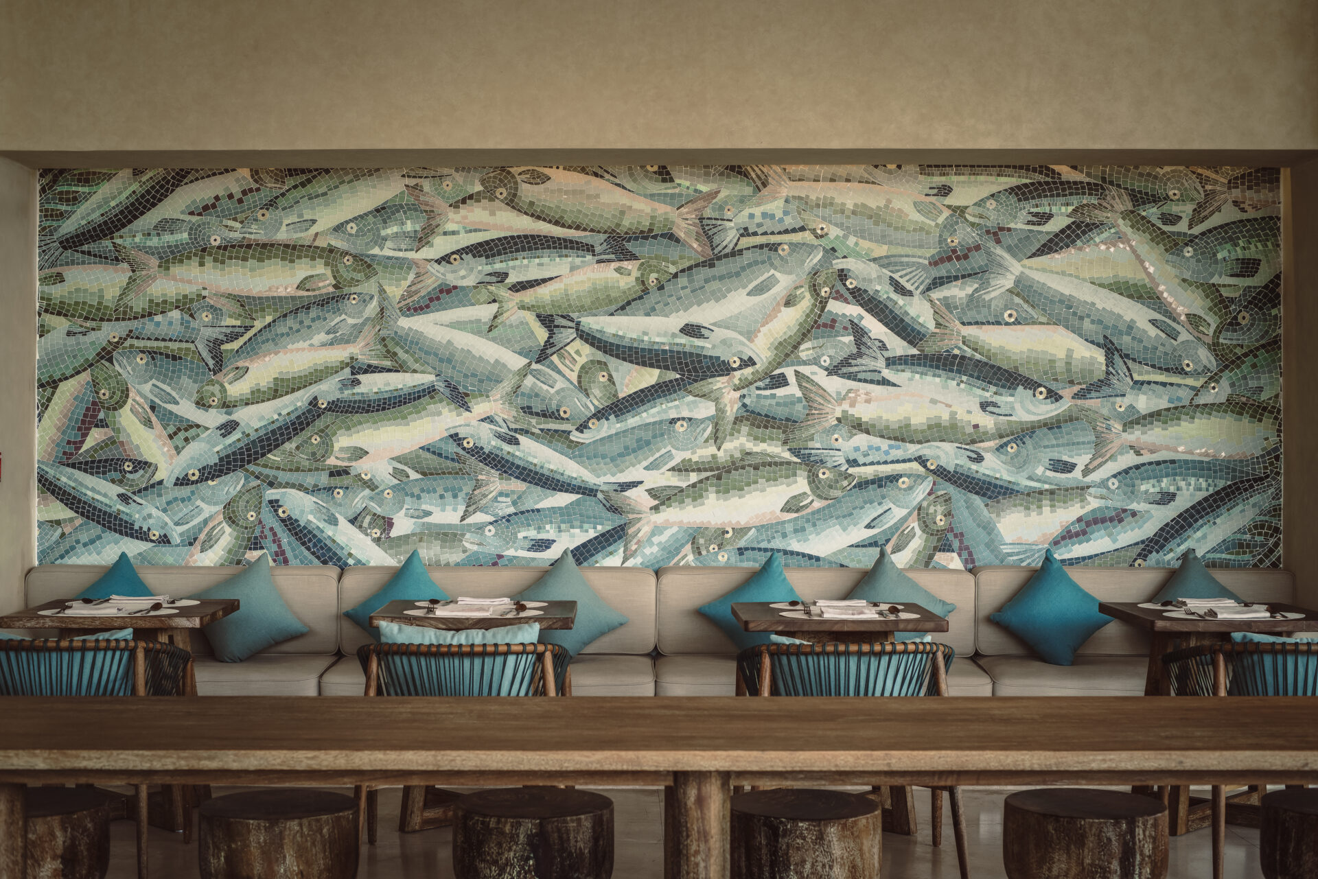 Artistic dining space at Namia River Retreat with ocean-inspired mosaic wall, blue cushions, and natural wooden tables.