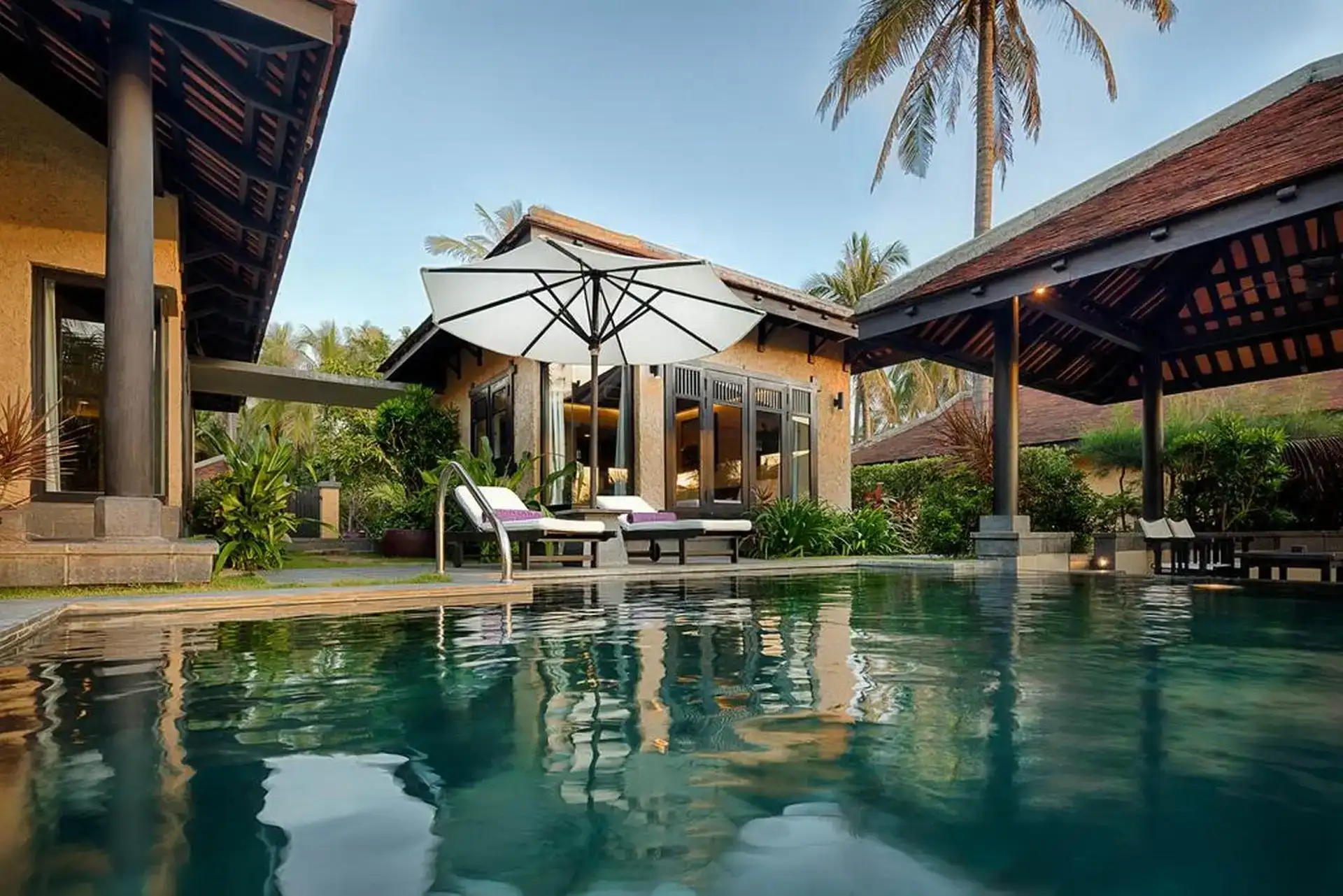 Tropical villa pool with sun loungers and palm-shaded pavilions at Anantara Hoi An Resort luxury retreat.