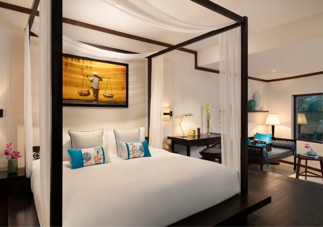Romantic canopy bed and tropical interiors with local art in a suite at Anantara Hoi An Resort.