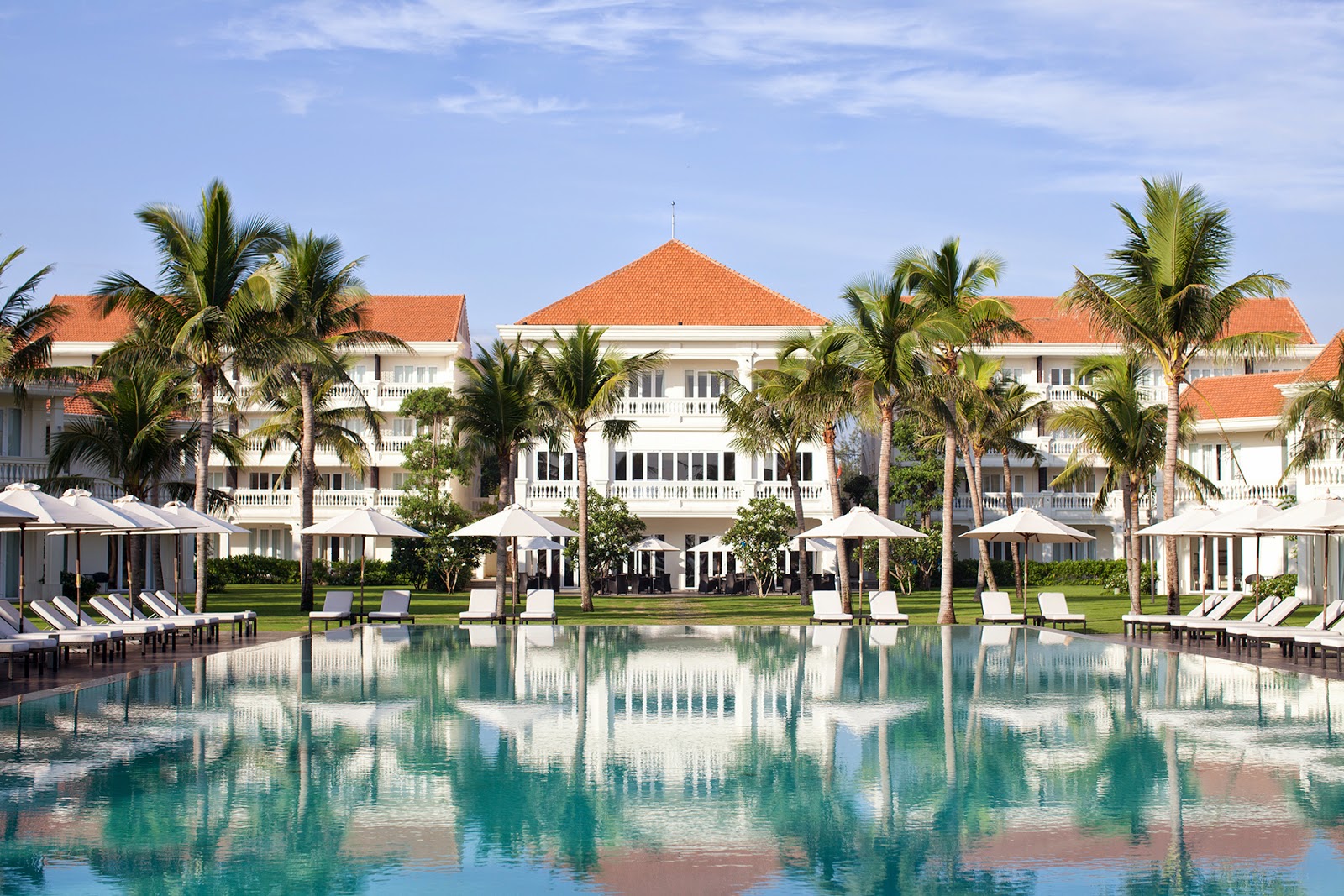 Large turquoise swimming pool with sun loungers, tropical palms, and garden views at Boutique Hoi An Resort.