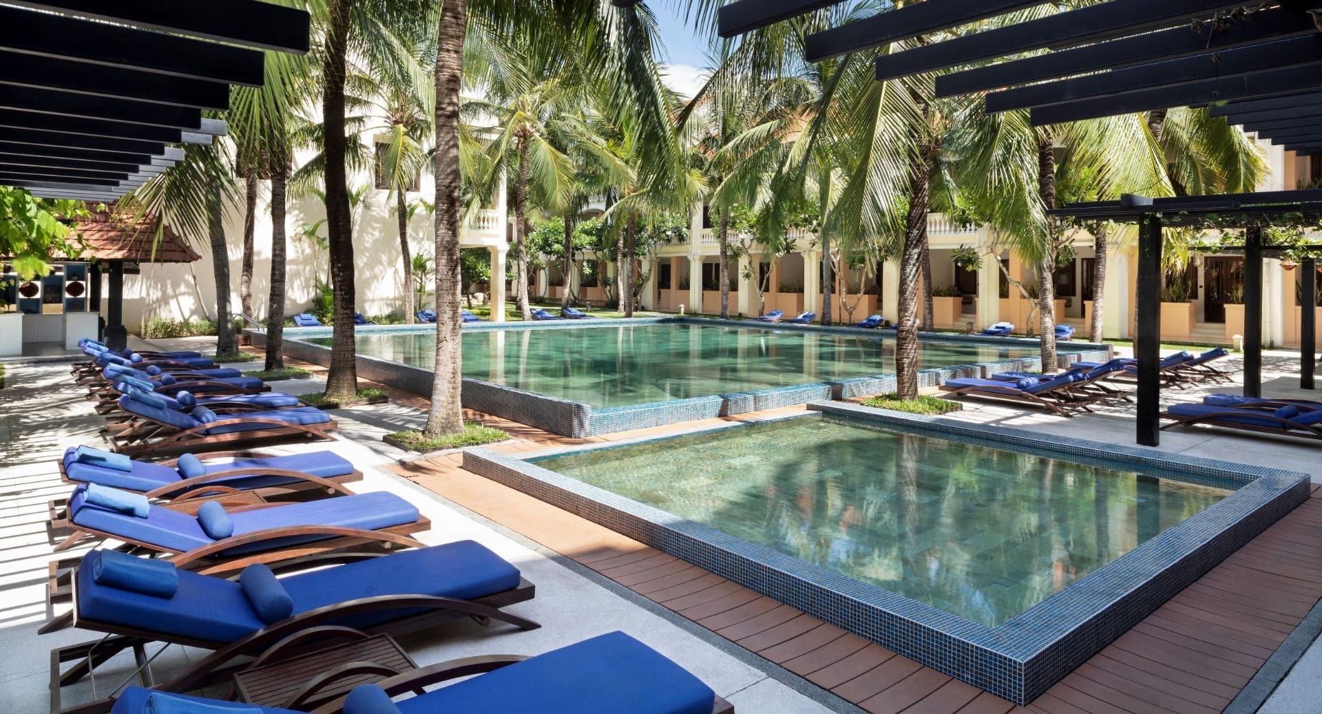 Tropical swimming pool surrounded by palm trees and blue sun loungers at Anantara Hoi An Resort Vietnam.