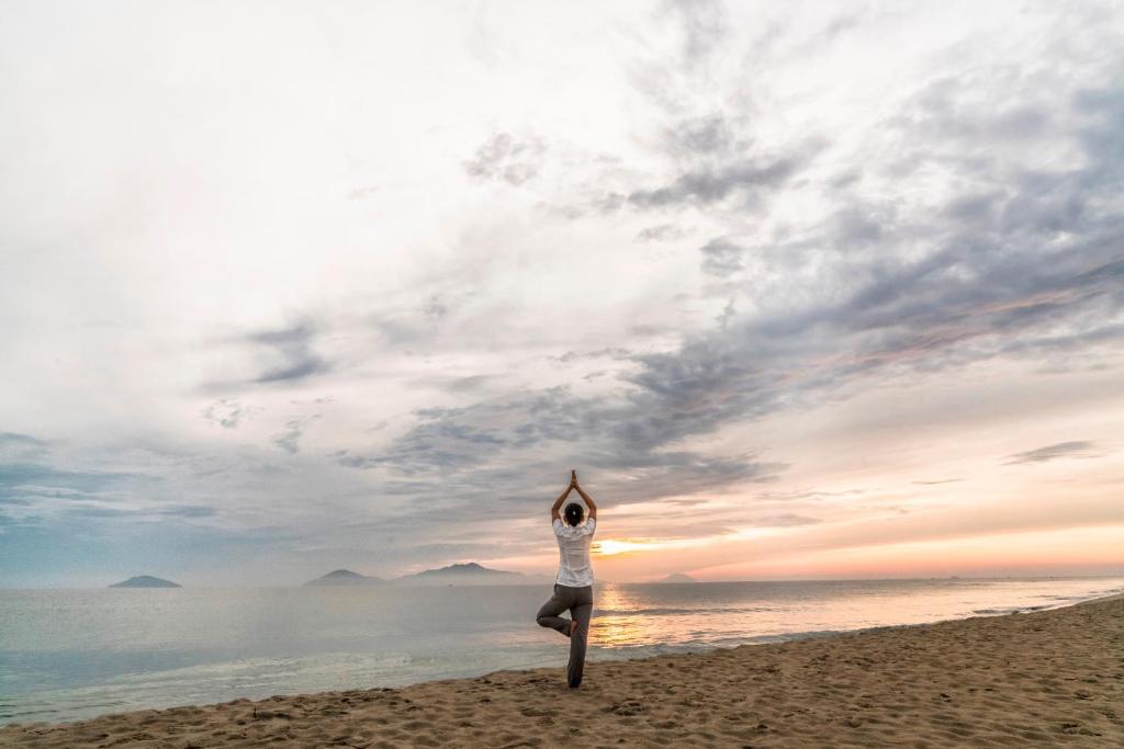 Guest practicing sunrise yoga on the sandy beach with ocean view and calm horizon at Boutique Hoi An Resort.