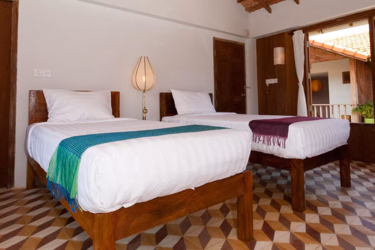 Room with two single beds and a balcony at Bambu Battambang Hotel.