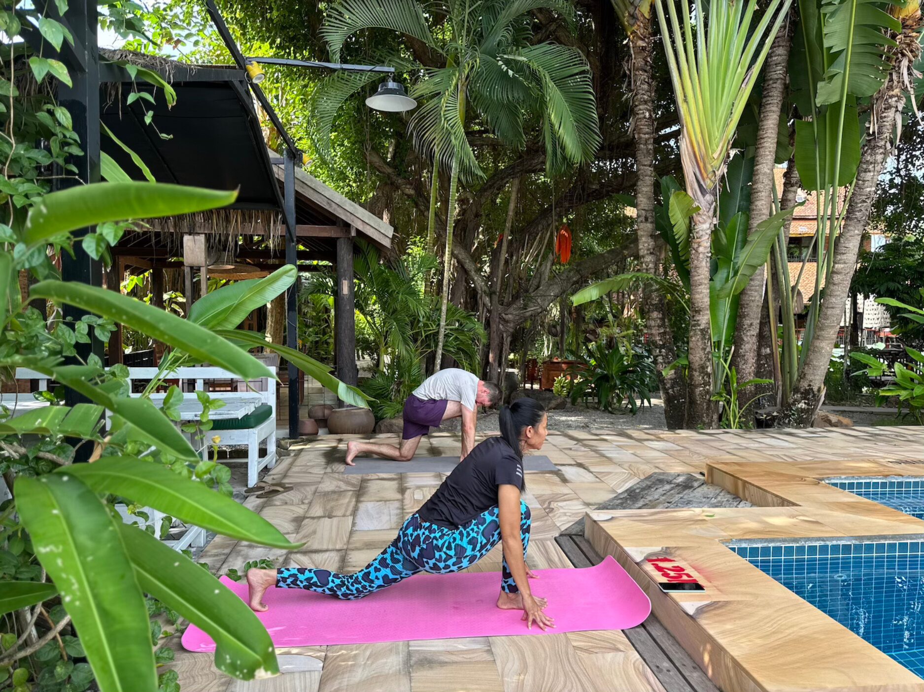 Outdoor yoga by the pool, amidst lush tropical gardens at the tranquil Maisons Wat Kor resort.